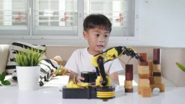 Uzaktan kumandayla tahta bloğu kaldırmak için robot kolu kullanan mutlu Asyalı çocuk, eğlenceli çocuk, başarılı bir ders kontrolü robot kolu, teknoloji bilimi eğitimi alıyor.
