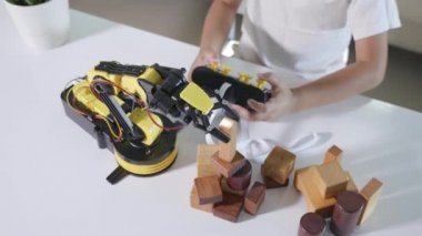 Uzaktan kumandayla tahta bloğu kaldırmak için robot kolu kullanan mutlu Asyalı çocuk, eğlenceli öğrenme başarılı bir ders kontrol robotu kolu, teknoloji bilimi eğitim konsepti.