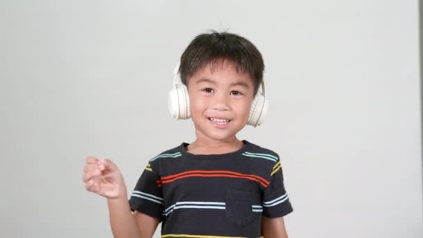 6岁的小可爱男孩在录音室里用无线耳机听音乐 在白色背景下拍摄 快乐的亚洲孩子在听音乐和跳舞 娱乐生活方式 — 图库视频影像