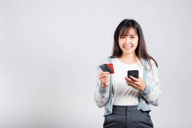 Gülümseyen bir kadın cep telefonu ve kredi kartı ile ödeme stüdyosu için kredi kartı, izole edilmiş beyaz arka plan, akıllı telefon alan ve online alışveriş yapan mutlu genç kadın.