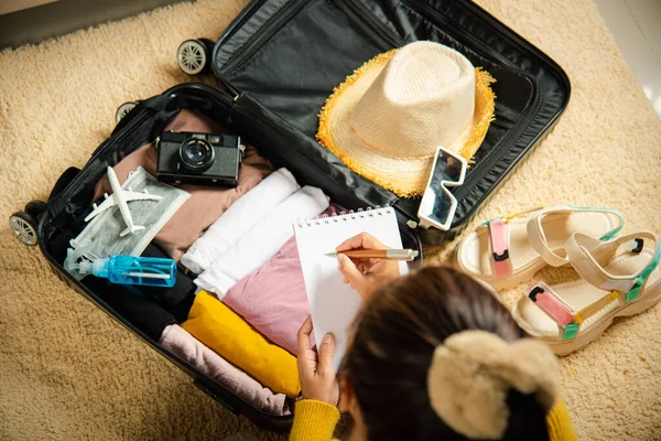 把旅行时需要打包的东西列一张清单 女人写信时 带着便条和手提箱到度假时 把便条放在房间里 准备好衣服放进行李箱 去度假 — 图库照片