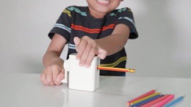 Küçük sevimli çocuk 5-6 yaşlarında. Stüdyo çekimleri sırasında kalem açacağı kullanırken gülümsüyor. Beyaz arka planda izole edilmiş, Asyalı çocuklar okul öncesi renk kalemleri, eğitim konsepti.