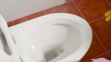 Sıvı sprey ve pembe bez kullanarak klozet kapağını temizleyen kadın evdeki tuvaleti siliyor, sarı lastik eldivenler takan kadın oturuyor ve klozet temizleyici tuvalet temizleyicisi, sağlık hizmetleri konsepti.
