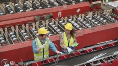Endüstriyel metal çarşaf fabrikasında makine bakımı yapan bir güvenlik kıyafeti giyen mühendis ve operatör, ekip çalışanı, öğretim görevlisi arkadaşının fabrikada ağır makineyi birçok ekipmanla kontrol etmesine yardım ediyor.
