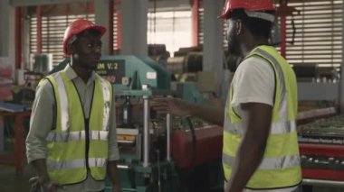 Metal çarşaf fabrikasında güvenlik üniforması giyen iki Amerikalı işçi el sıkışırken mühendis endüstriyel alanda el sıkışırken...