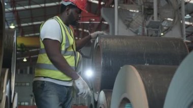 İki siyah işçi fabrika mühendisi tekstil teftişi ve depodaki metal kaplama malların envanter seviyelerini kontrol ediyorlar. Birlikte konuşuyorlar ve nakliyeye hazır ürünlerle çalışıyorlar.