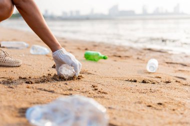 Plajı temizlemek için plastik poşet içine plastik şişe karıştıran gönüllü bir kadın, çöpleri temizleyen bir kadın, ekoloji konsepti ve Dünya Çevre Günü, Dünya 'yı Kurtarma Günü.