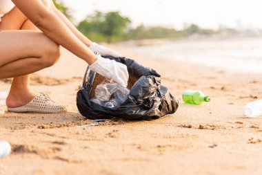 Plajı temizlemek için plastik şişeyi çöp poşetine atan gönüllü bir kadın, gün batımında çöpleri temizleyen bir kadın, ekoloji konsepti ve Dünya Çevre Günü, Dünya 'yı Kurtarma Günü.