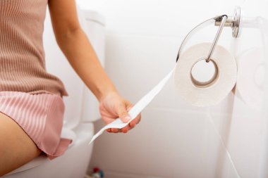 Kapalı el tuvalet kağıdını silmek için tutacağı çekiyor. Tuvalette oturan kadın beyaz mendili alıp duvardan havluya döküyor. Sağlık sigortası konsepti.