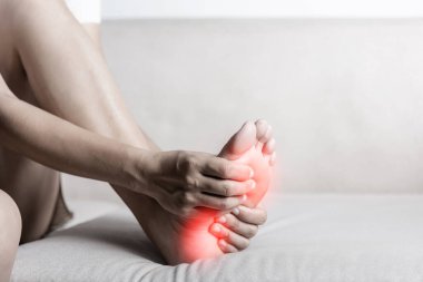 Ayak ağrısı, kanepede oturan Asyalı bir kadın evinde ayağında ağrı, ayak ağrısı çeken bir kadın. El masajı kullan. İç taban kaslarını gevşet.