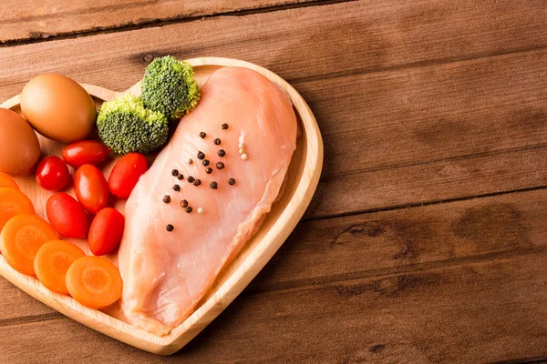 生鸡胸肉片的头像没有无骨与香料迷迭香 胡萝卜和鸡蛋在心脏板木木制背景 健康的食物日的概念 — 图库照片