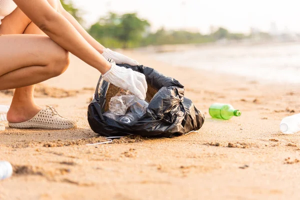 Plajı temizlemek için plastik şişeyi çöp poşetine atan gönüllü bir kadın, gün batımında çöpleri temizleyen bir kadın, ekoloji konsepti ve Dünya Çevre Günü, Dünya 'yı Kurtarma Günü.
