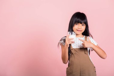 Asyalı küçük çocuk 10 yaşında gülümsüyor süt bardağı içiyor beyaz süt içiyor ve pembe arka planda izole edilmiş stüdyo çekimlerini işaret ediyor mutlu çocuk günlük sağlık sigortası yemekleri