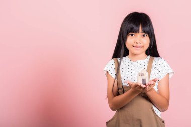 Asyalı küçük bir çocuk. 10 yaşında. Stüdyoda ahşap ev modeli. Pembe arka planda izole edilmiş.