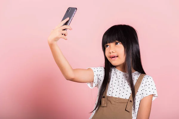 ピンクを背景にしたスタジオ撮影で携帯電話で自撮りを楽しむアジアの子供10年 スマートフォンでビデオ自撮りをする幸せな子供のライフスタイル — ストック写真