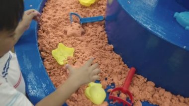 Mutlu Asyalı çocuklar eğlence merkezinde eğleniyor. Şişme kale karantinada kinetik kum oynuyor. Heyecanlı çocuk zıplama evlerinde kum ve kum havuzu oynuyor.