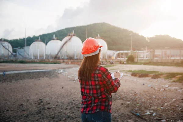 Petroleum Engineers. Happy Asian worker woman in oil chemical industry worker working visual inspection list on clipboard in plant, do Action of worker do safety checklist which is clipped