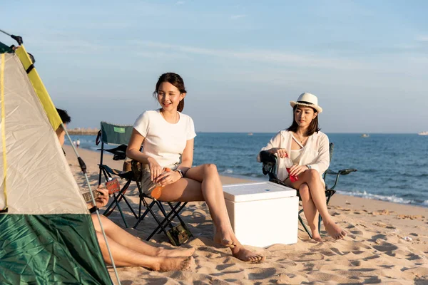 キャンプでのドリンクと幸せな友人やキャンプテントの休暇時間の近くの砂のビーチでの休暇で一緒に笑って 夏の旅行で若いアジアのグループの女性と男屋外 — ストック写真