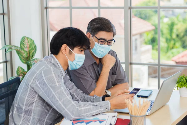 Asian young man teaching senior father how to use credit card for shopping online with laptop computer in the living room, adult son holding bank card helping Dad to purchases web online application