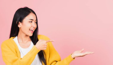 Asyalı güzel bir kadın gülümsüyor pembe arka planda parmakla işaret ediyor, Taylandlı mutlu kadın yüzü boş bir yere bakıyor metin için fotokopi alanından uzaklaşmaya çalışıyor.