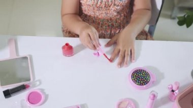 Asyalı sevimli komik küçük kız makyaj malzemelerini şişeye bandırıyor oje sürmek için kırmızı oje sürüyor, kadın olmak için etkinlik öğreniyor, mutlu çocuk güzel makyaj oyuncağıyla makyaj yapıyor.