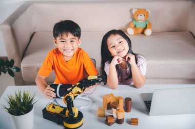 Two children programming and testing robot arm their science, Kid little girl program code to robot with laptop computer and the boy test with remote control to pick up wood block, education lesson
