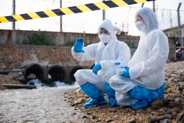 Nehirden gelen suyu test tüpü, koruyucu giysi içindeki bilim adamı veya biyolog ile örnekleyen ve maskesini koruyan ekolojist, analiz için endüstriden atık su örneği topluyor, sorun ortamı