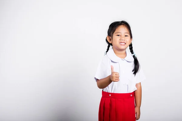亚洲可爱的小屁孩喜笑颜开穿着学生制服红裙子在工作室里露出大拇指无拘无束地拍着白色背景的照片 人物形象的小女孩在幼儿园 小孩回到学校 — 图库照片