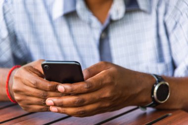 Mutlu Asyalı siyah iş adamı elinde modern dijital akıllı telefon boş ekran aygıtı teknolojisi tutuyor ve kafeteryadaki internet bağlantısını kuruyor.