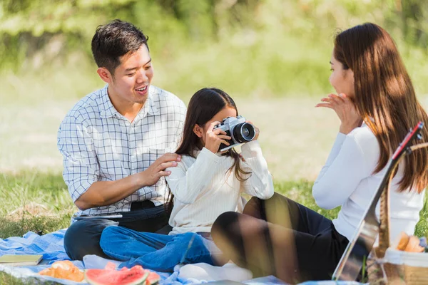幸せなアジアの若い家族の父 母と子供の女の子楽しい屋外ピクニックを楽しみながら 晴れた日に庭の公園でレトロなカメラでピクニックブランケット撮影写真に座っています — ストック写真