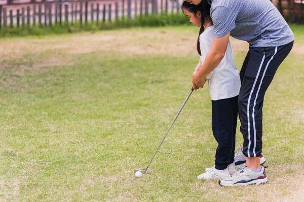 Asian young father support teaching training daughter to play perfect golf while standing in the game of golf together in nature a field garden park, family outdoors sport concept