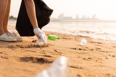 Plajı temizlemek için plastik poşet içine plastik şişe karıştıran gönüllü bir kadın, çöpleri temizleyen bir kadın, ekoloji konsepti ve Dünya Çevre Günü, Dünya 'yı Kurtarma Günü.