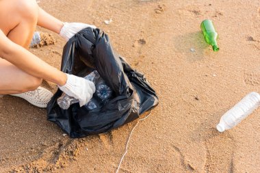 Plajı temizlemek için plastik poşet içine plastik şişe karıştıran gönüllü bir kadın, çöpleri temizleyen bir kadın, ekoloji konsepti ve Dünya Çevre Günü, Dünya 'yı Kurtarma Günü.