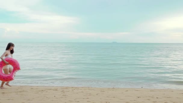美丽的亚洲女人带着橡皮圈在沙滩上奔跑 穿着比基尼的快乐女人在热带海滩度假度假度假度假 在暑假放松身心 — 图库视频影像