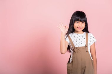 Asyalı küçük bir çocuk, 10 yaşında. Stüdyoda işaret dilinde iyi bir jest yapıyor. Pembe arka planda izole edilmiş.