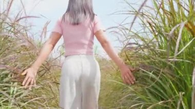 Bulanık elleri tarlada çimenlere dokunuyor, çayırlarda çiçeklerle yürüyen güzel bir kadın, yakın el, doğa tatili ve sağlıklı güneş yaşam tarzı.