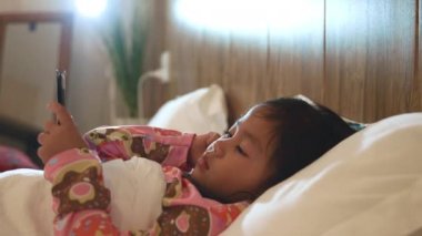 Çocuk yatak odasında video ve çizgi film izliyor, küçük Asyalı kız yatak bağımlısı oyun ve çizgi film üzerinde dijital tablet oynuyor, internet komik konsepti var.