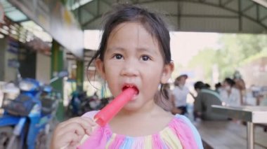 Yazın buzlu dondurma yiyen mutlu Asyalı küçük kız, dışarıda donmuş meyveli dondurma yerken komik surat yapan genç kadın çocuk, dondurmayla rahatlarken eğlenen çocuk.