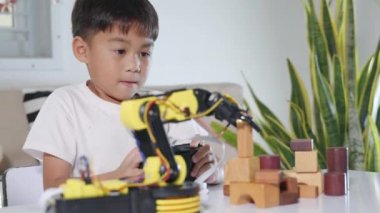 Uzaktan kumandayla tahta bloğu kaldırmak için robot kolu kullanan mutlu Asyalı çocuk, eğlenceli çocuk, başarılı bir ders kontrolü robot kolu, teknoloji bilimi eğitimi alıyor.