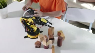 Uzaktan kumandayla tahta bloğu kaldırmak için robot kolu kullanan mutlu Asyalı çocuk, eğlenceli çocuk, başarılı bir ders kontrolü robot kolu, teknoloji bilimi eğitimi alıyor.