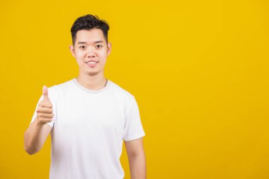 Asyalı yakışıklı genç adam pozitif gülümsüyor. İyi bir hareket gösteriyor. Ya da kameraya bakan bir işaret gibi.