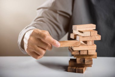 Alternatif risk planı. İş adamı kule blokları oyunu oynuyor, adam bir tahta bloğu kuleden çekiyor yumruğunu sıkıyor, bunu başarmaktan büyük keyif alıyor, iş büyütme konsepti.