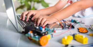 Asyalı çocuk, Arduino robot arabası için dizüstü bilgisayarla kodlama ve programlama öğreniyor, küçük çocuk öğrenciler, bilgisayar kullanarak araba oyuncağıyla kod yazıyorlar, STEAM eğitim yapay zeka teknolojisi kursu.