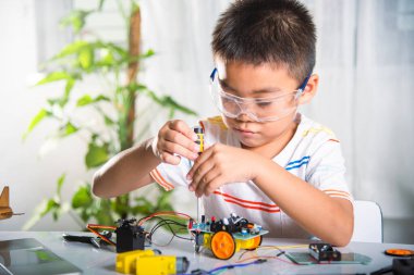 Küçük çocuk oyuncağı monte etmek için tornavidayla cevizi sıkıyor, Asyalı çocuk evde Arduino robot araba ev ödevi yapıyor, eğitim yapay zeka atölyesi dersi öğreniyor.