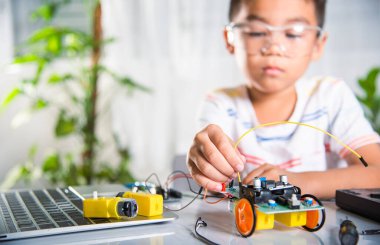 Küçük çocuk kod göndermeden önce oyuncakla uzaktan öğreniyor, Asyalı çocuk Arduino robot arabasıyla sensör çipine enerji ve sinyal kablosu takıyor, STEAM eğitim teknolojisi kursu.