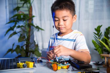 Asyalı çocuk, Arduino robot arabasıyla sensör çipine enerji ve sinyal kablosu takıyor, küçük çocuk oyuncaklarla uzaktan öğreniyor, STEAM eğitim teknolojisi dersleri.