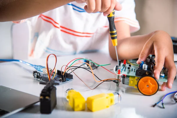 Little child tighten the nut with a screwdriver to assemble car toy, Asian kid boy assembling the Arduino robot car homework project at home, education AI technology workshop school learning lesson