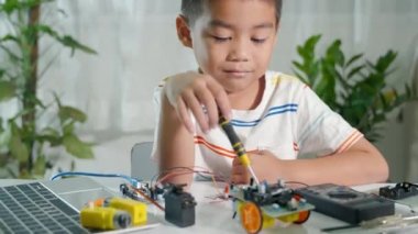 Asyalı çocuk Arduino robot araba ev ödevi projesini evde yapıyor, Küçük çocuk oyuncağı monte etmek için tornavidayla fındığı sıkıyor, elektronik yapay zeka atölyesi dersi oluşturuyor.