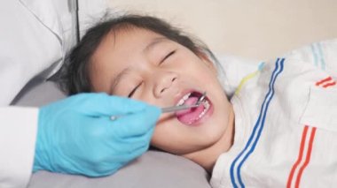 Diş hekimi çocuk sağlık muayenesi. Küçük tatlı kız için muayene prosedürü uygulayan Asyalı dişçi küçük çocuğun ağız boşluğunu muayene ediyor diş boşluğunu kontrol etmek için ağız aynası kullanıyor.