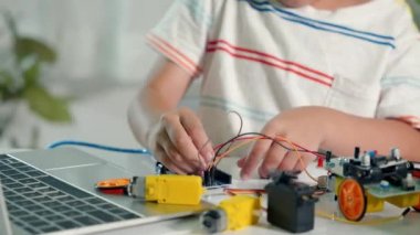 Asyalı çocuk, Arduino robot arabasıyla sensör çipine enerji ve sinyal kablosu takıyor, küçük çocuk oyuncaklarla uzaktan öğreniyor, STEAM eğitim teknolojisi dersleri.